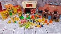 Overview of the vintage Fisher-Price playsets: Main Street building, Family Farm barn, Pet Family House, along with many Fisher-Price figures, chairs, tables, vehicles, and accessories scattered on a lace cloth background.