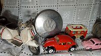 Photo showing the white vintage scooter model with number 8, red and pink Volkswagen Beetle toy cars, the Fisher Price Volkswagen mini bus, and a Volkswagen hubcap.