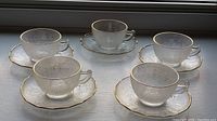 Five Jeannette Glass cups placed individually on matching saucers arranged on window sill showing front view.