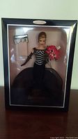 Full view of Barbie doll in original box displaying black gown, silver glitter detailing, and bouquet of pink roses held by doll.