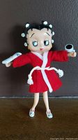 Front view of Betty Boop doll wearing red robe, holding newspaper and cup, showing overall appearance and accessories.