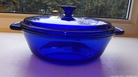 Full side view of the cobalt blue casserole dish with lid on, showing shape, handles, and glass color.