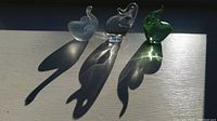 Three elephant figurines: clear crystal, frosted with blue specks, and green glass, casting shadows on a surface