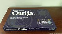 Top view photo of the glow in the dark Ouija board box showing branding, age suitability, and included contents.