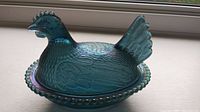Front view of the hen on nest covered dish highlighting the shape and iridescent blue color