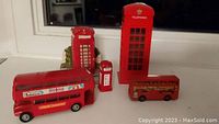 Photo showing the two vintage London doubledecker bus models and three red British telephone booth models in varying sizes and materials on a white surface.