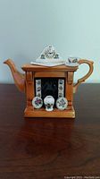 Full front view of the ceramic miniature fireplace teapot with clock on mantle, floral tile detailing and small ceramic vases on the hearth area.