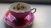 Side view of the pink floral teacup on matching saucer showing gold trim on edges, handle and foot.