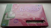 Photo of the front of the pink Scrabble Designer's Edition box showing branding, rotating gameboard feature, and Toys R Us exclusive logo.