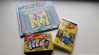Photo of Simpsons Xmas Book, UNO Simpsons Special Edition tin card game, and Simpsons video cassette of The Simpsons Game for PSP