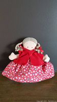Front view of Topsy Turvy doll featuring Little Red Riding Hood with red cape and floral skirt on wooden surface against grey wall.