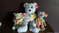 Three Ty Beanie Bears, Bloom (white multicolor floral), Peace (tie-dye pastel with peace symbol), and Cherry (green/pink tie-dye with butterfly), each with Ty tag visible.