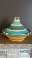 Full side view of tagine pottery bowl showing striped terracotta colors, conical lid, and round base.
