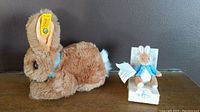 Side view of the brown Steiff rabbit plush with yellow Steiff ear tag and the mini Peter Rabbit by Eden Toys in original box