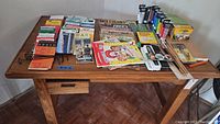 Full view of the drafting table top with an assortment of craft paints, brushes, a box of Crayola items, and numerous travel brochures.