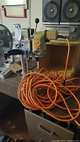 Full view of the Black and Decker drill press sitting on a table with a coiled orange power cord.