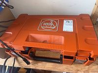 Closed orange hard plastic case with carrying handle and Fein logo on lid