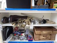 Fishing gear items displayed on a shelf including brown boots, camouflage gloves, spools of fishing line, small fishing accessories, and two brown tackle boxes stacked.