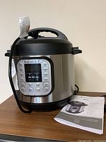 Front view of Instant Pot Duo with control panel and manual beside it