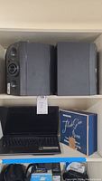 Photo showing Acer laptop under pair of black Boston speakers and Minori Flash Gun Junior box on shelf.