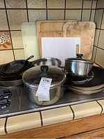 Skillets, pots, and cutting boards on kitchen countertop showing full lot contents.