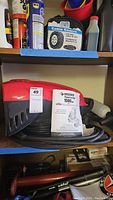 Husky power washer attachment with red and black housing, power cord coiled, and operator's manual on shelf.