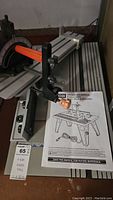 Image showing the full router table surface, adjustable fence with black knobs, orange handle on miter gauge, and included user manual.