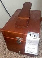 Front view of the rectangular wooden shoe shine box showing metal latch and handle on top.