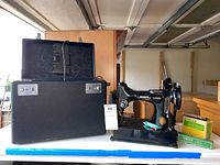 Singer sewing machine displayed next to black carrying case and accessory boxes.