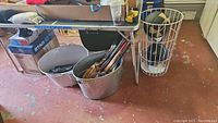 Wide shot of sports equipment under table including tubs with bats and gloves.