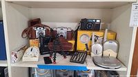 Shelf view of cameras, audio player, baby monitors, timer, calculator, tripod