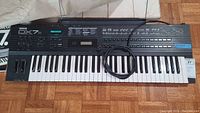 Top-down view of Yamaha DX7s synthesizer showing full 61-key keyboard, pitch and modulation wheels, control panel, attached power cable.