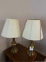 Pair of two brass tri-lamp style table lamps on wooden table with cream colored shades.