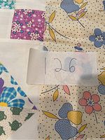 Close-up of patchwork quilt fabric showing floral and teapot patterns with a tag labeled 126.