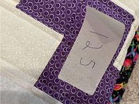 Purple geometric patterned quilt folded showing sewing tag with hand written 25