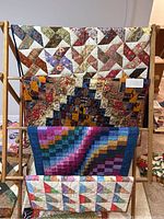 Full view of four handmade rectangular quilts on a quilt rack showing pattern and color variety