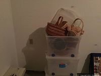 Stack of three clear plastic storage totes with the top tote containing various woven baskets inside.