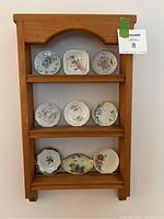 Full view of the wooden display shelf holding nine ceramic butter pats arranged on three shelves.