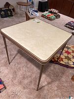 Overall view of the beige metal folding card table with off-white marbled top in a room setting.