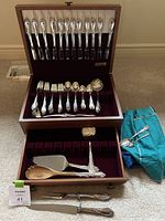 Open wooden chest showing velvet-lined slots with 12 knives in upper tray, forks and spoons in lower tray, plus serving utensils displayed outside