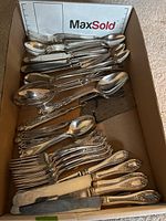 Top view of a box with mixed flatware including forks, spoons, and knives showing different handle patterns.