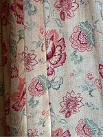 Close-up photo showing the floral patterned fabric of the drapes with pink flowers, green leaves, and beige background.