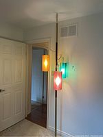 Full view of the mid century modern floor to ceiling lamp installed in a corner with the three colored acrylic shades lit: orange, red, and teal.
