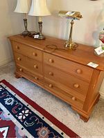 Full view of long pine dresser with six drawers and wooden knobs, with lamps on top.
