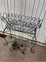 Full view of the large and small black metal plant stands together in room with light curtains.