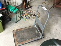 Full view of metal flat platform hand truck dolly on a concrete floor, showing the flat base with rust and a curved handle.