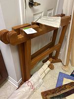 Wooden quilt frame leaning against the wall, visible lectured note on top of it. Frame is varnished wood with carved ends and supportive cross beams.