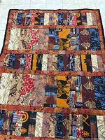Quilt with rectangular patches of various abstract prints in earth tones such as orange, brown, red and blue with circular patterns bordering patches