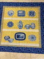 Blue and yellow quilt with printed blue and white tea service patterns on yellow background and floral borders