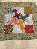 Quilt square with four multicolored autumn leaves center and floral printed corners